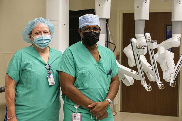 Surgeons in green scrubs and masks standing in front of surgical robot