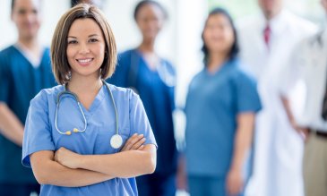 Medical professionals wearing scrubs looking and smiling at camera, one in focus. 