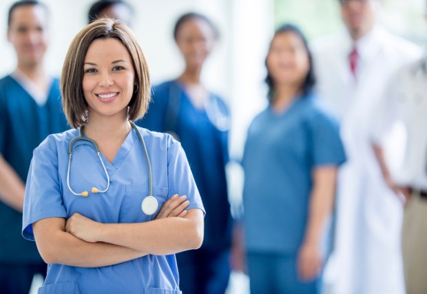 Medical professionals wearing scrubs looking and smiling at camera, one in focus. 