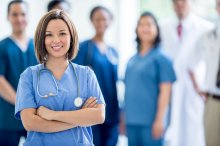 Medical professionals wearing scrubs looking and smiling at camera, one in focus. 