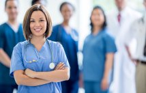 Medical professionals wearing scrubs looking and smiling at camera, one in focus. 
